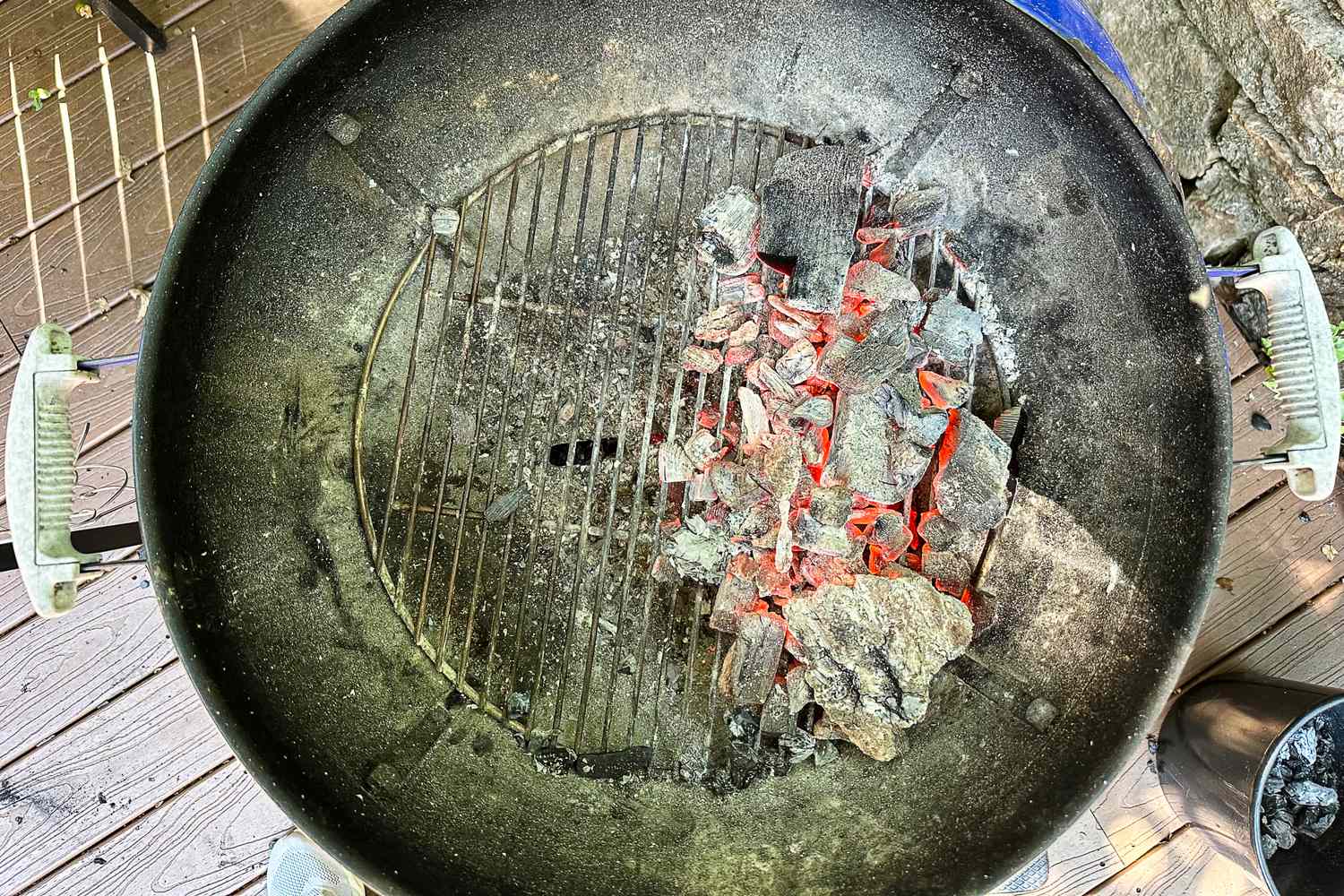A charcoal grill with glowing embers and ash on a wooden surface