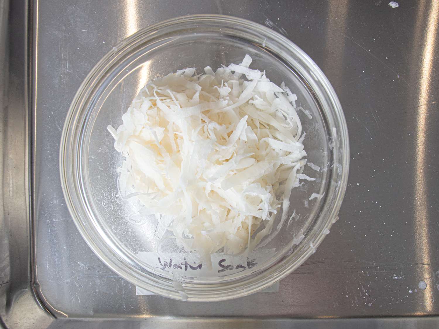 A bowl filled with shredded soaked potato placed on a metal tray