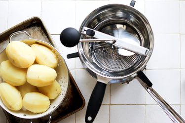 a food mill with boiled potatoes in a steamer basket on a white tile surface