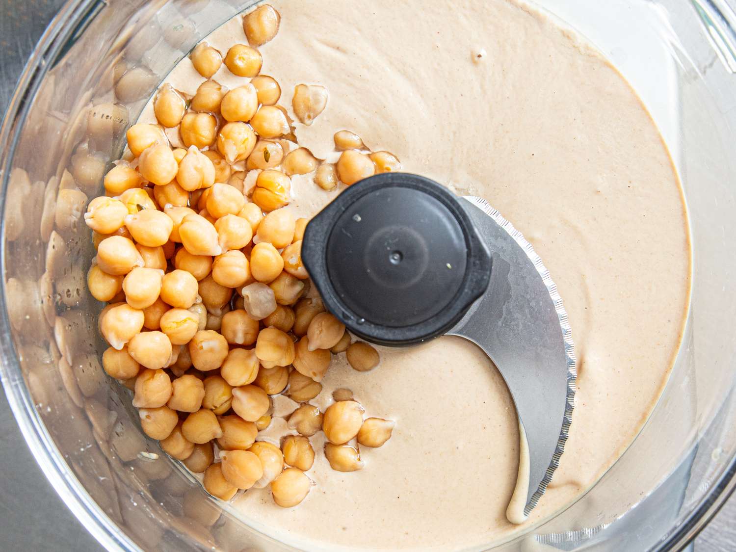 Ingredients for making hummus chickpeas and tahini in a food processor bowl with a blade