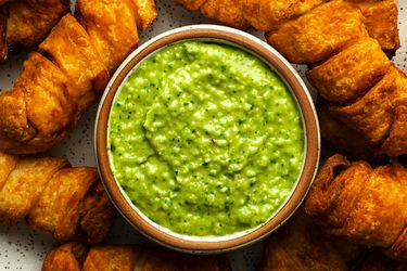 A close-up photo of a ceramic bowl holding guasacaca, surrounded by tequeÃ±os.