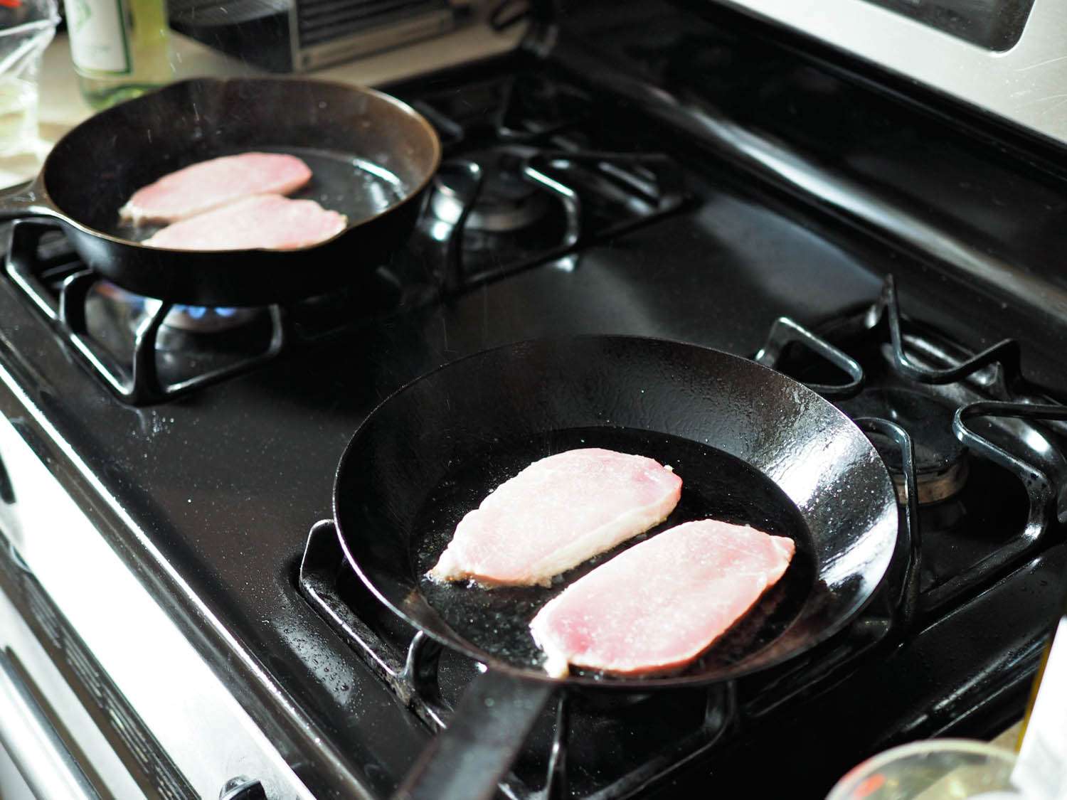 Pork frying in two black pans on stovetop