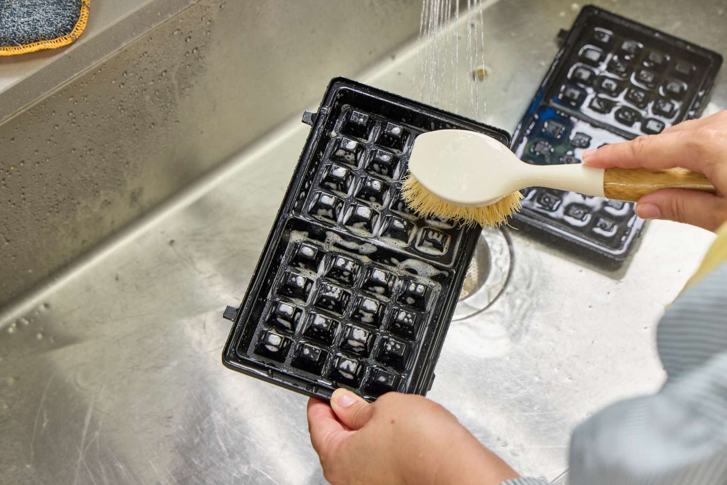 A person cleans the Black+Decker 3-in-1 WM2000SD Waffle Iron with a brush