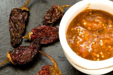 A small bowl of chile morita salsa next to some dried morita chiles. 