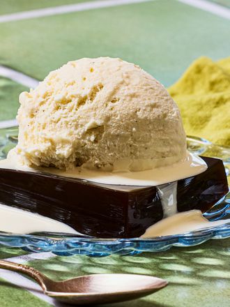 A dessert featuring a block of coffeeflavored gelatin topped with a scoop of ice cream and drizzled with cream on a glass plate