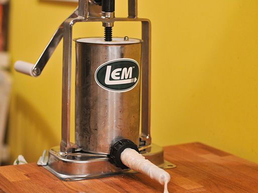 A metal Lem-brand sausage stuffer with a casing on the horn being filled.
