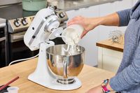 A person pours flour into the KitchenAid Classic Plus Series 4.5 Quart Tilt-Head Stand Mixer