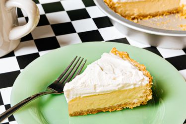 A slice of creamtopped pie on a green plate with a fork a pie plate with the rest of the pie in the background