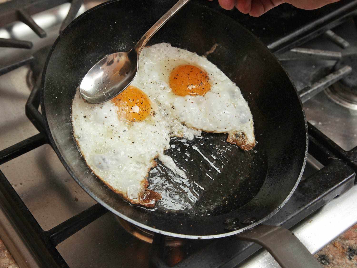 Spooning hot oil over frying eggs in a tilted skillet.