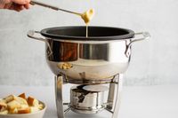 A person dipping a chunk of bread into cheese fondue in a fondue pot.