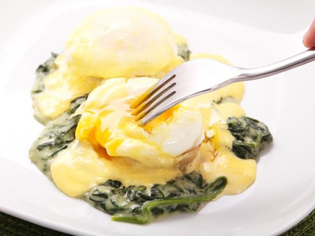 A white plate with eggs sardu--eggs Benedict on top of creamed spinach and artichoke hearts, topped with hollandaise sauce.