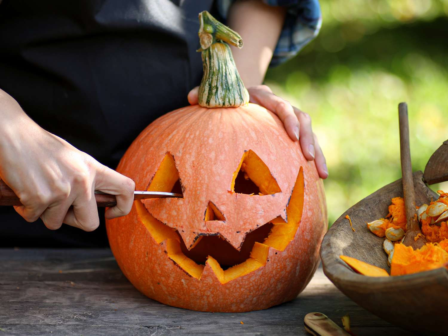 A person carving a jackolantern from a pumpkin on a wooden surface outdoors