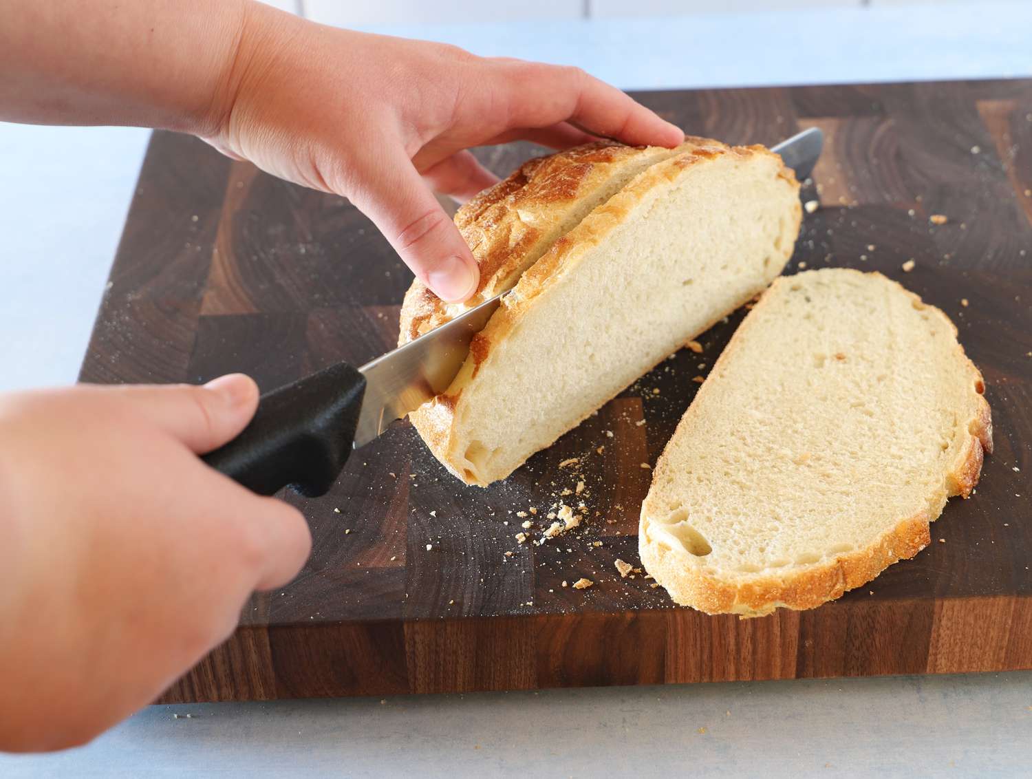 A person using a bread knife to slice a boule