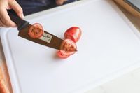A person thinly slicing tomatoes with a knife