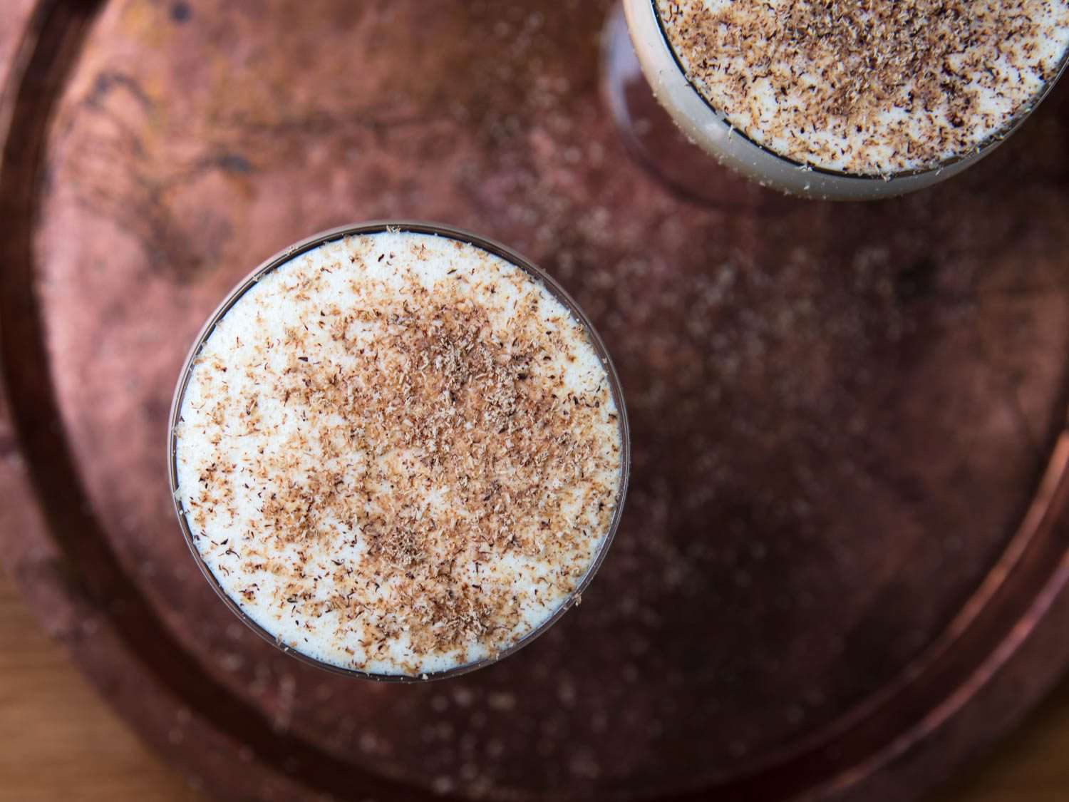 Overhead view of two goblets of eggnog, garnished with fresh nutmeg.