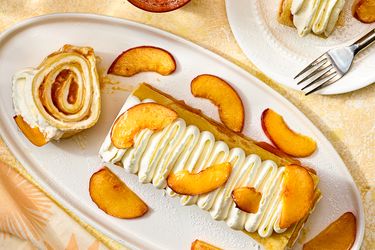 Plated dessert with rolled crepes sliced peaches and cream topping