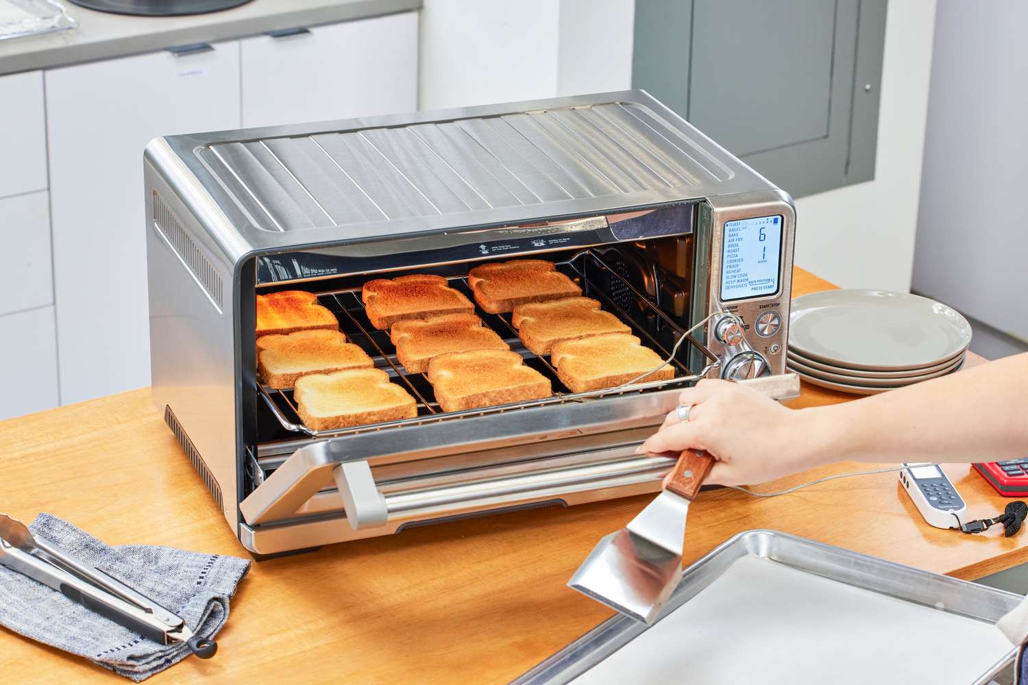 A person opening the Breville the Joule Oven Air Fryer Pro door while holding a spatula