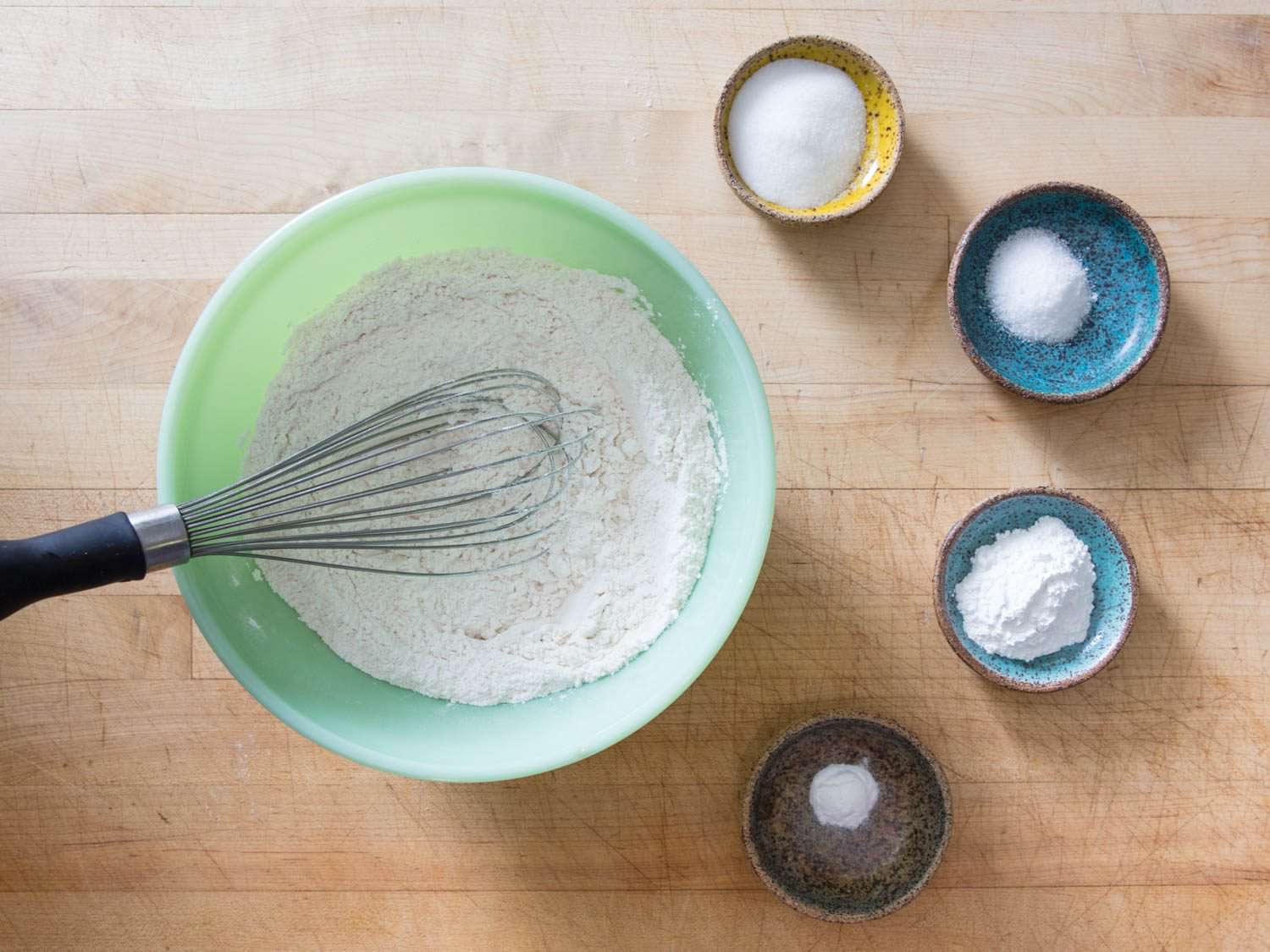 All-purpose flour, sugar, salt, baking powder, and baking soda in separate bowls on a work surface.