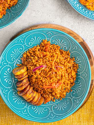 Overhead view of Jollof rice on a bright blue plate on top of a yellow table runner next to a glass of water