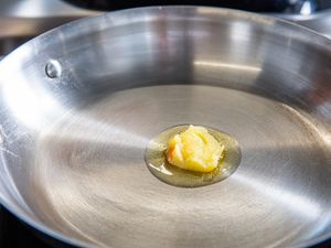 A piece of ghee melting in a stainless steel frying pan on a stove