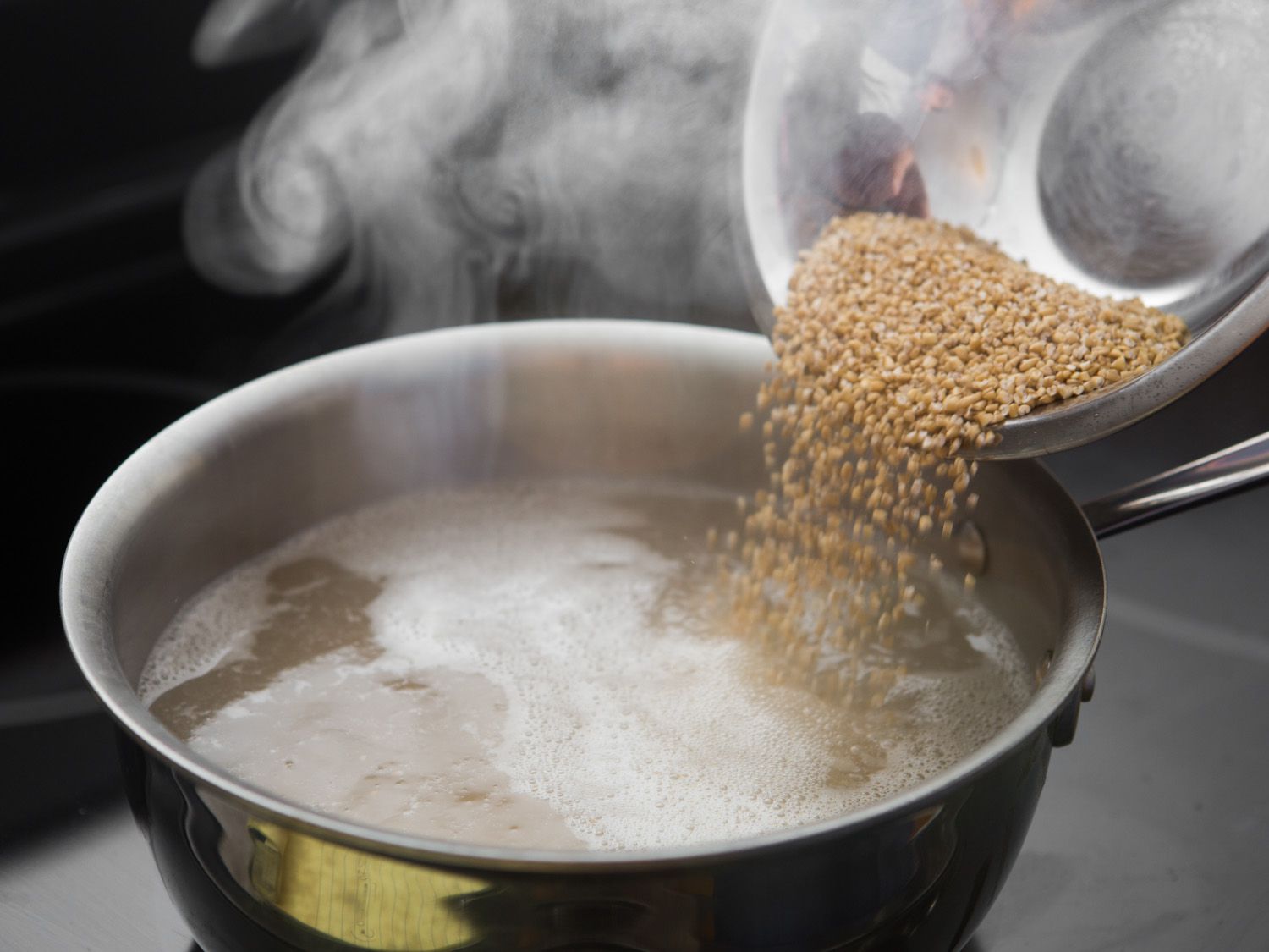 Steel-cut oats are added to a saucier of steaming water.