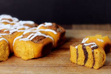 Pumpkin sweet swirl buns on a cutting board. One has been sliced in half to show the swirled layers of filling.