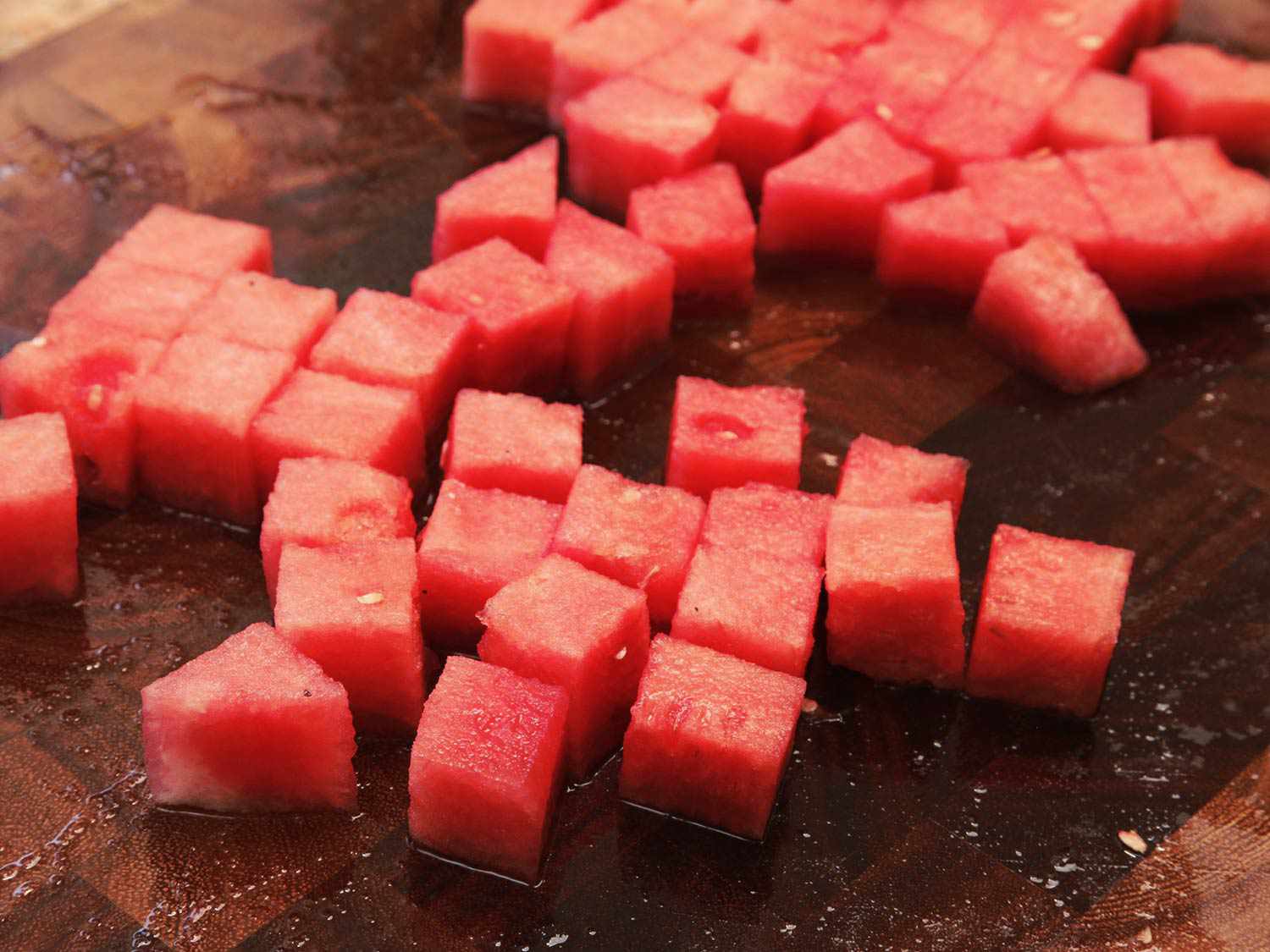Cubes of watermelon on a wooden cutting board.