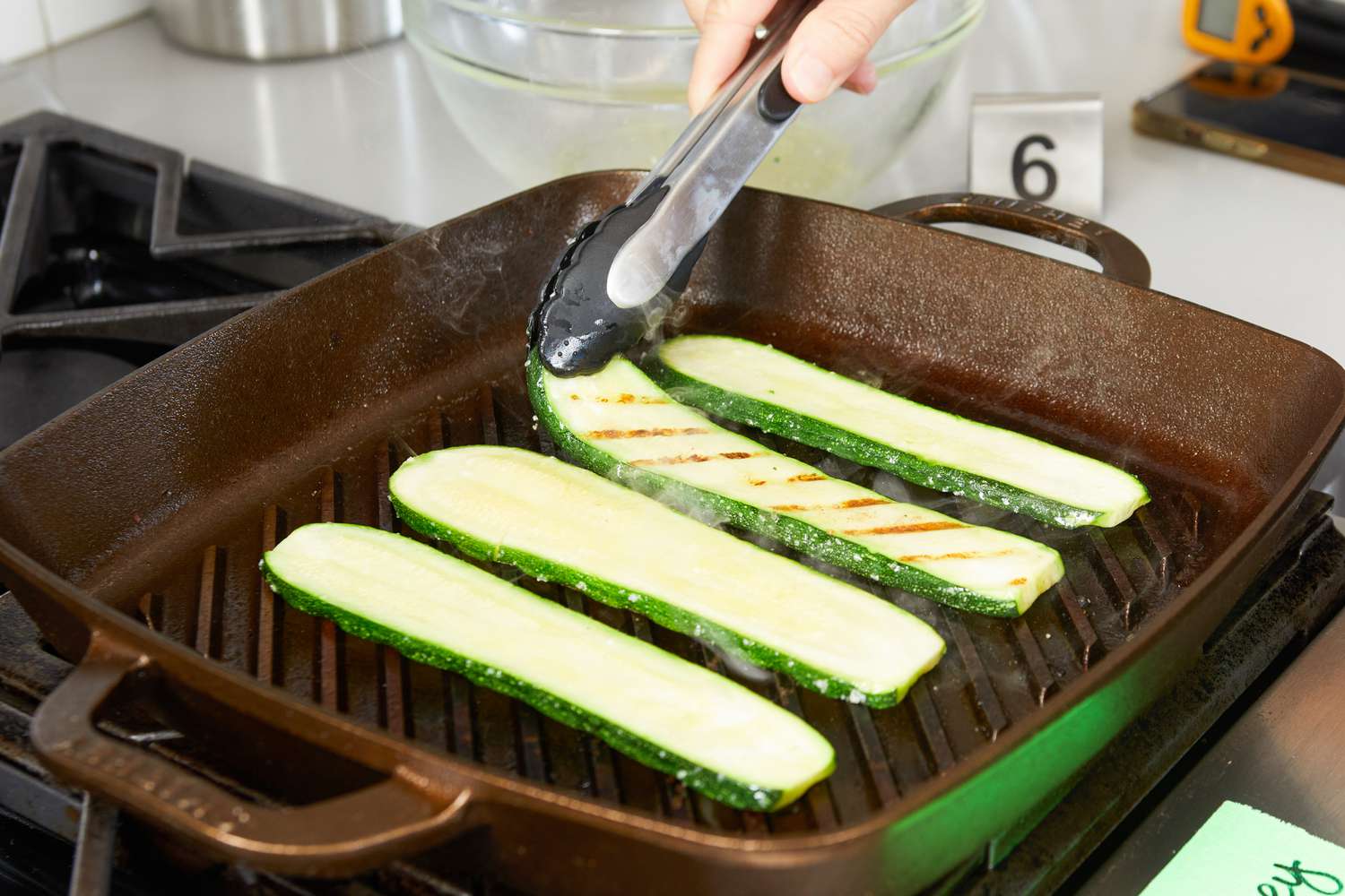 A person flipping zucchinis while they cook on the Smithey Ironware Co. No. 12 Grill Pan.