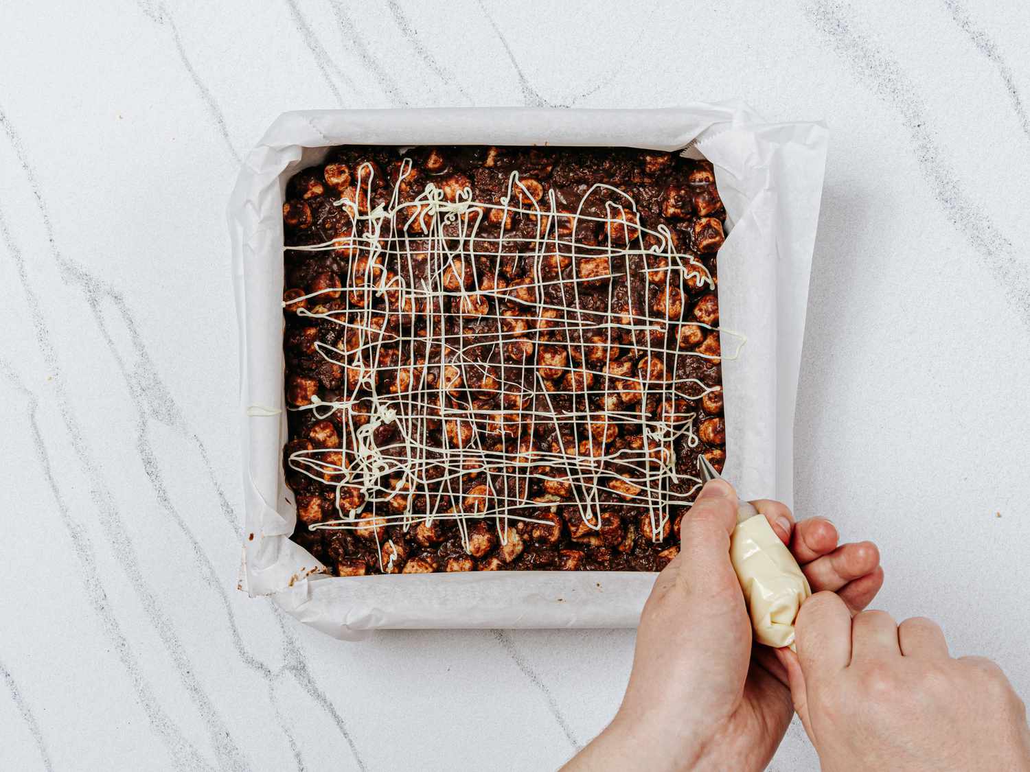 Drizzling rocky road pan with melted chocolate in a piping bag