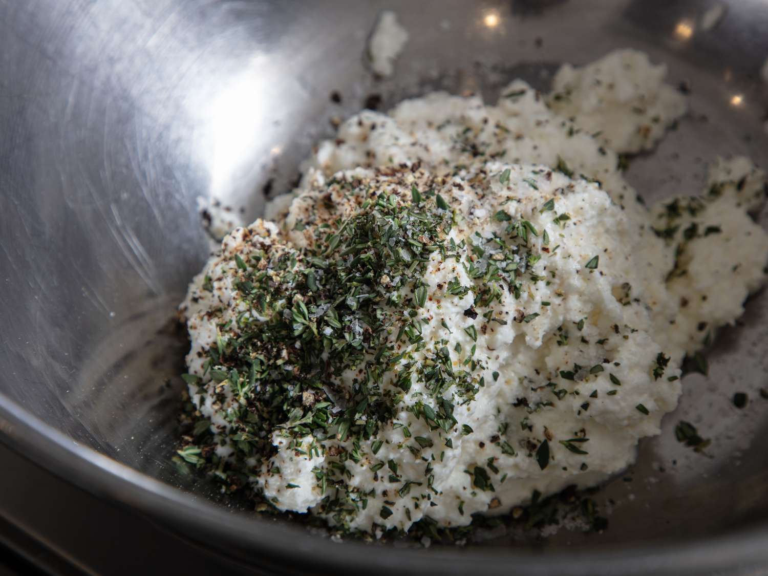 Ricotta cheese mixed with herbs and seasonings in a metal bowl