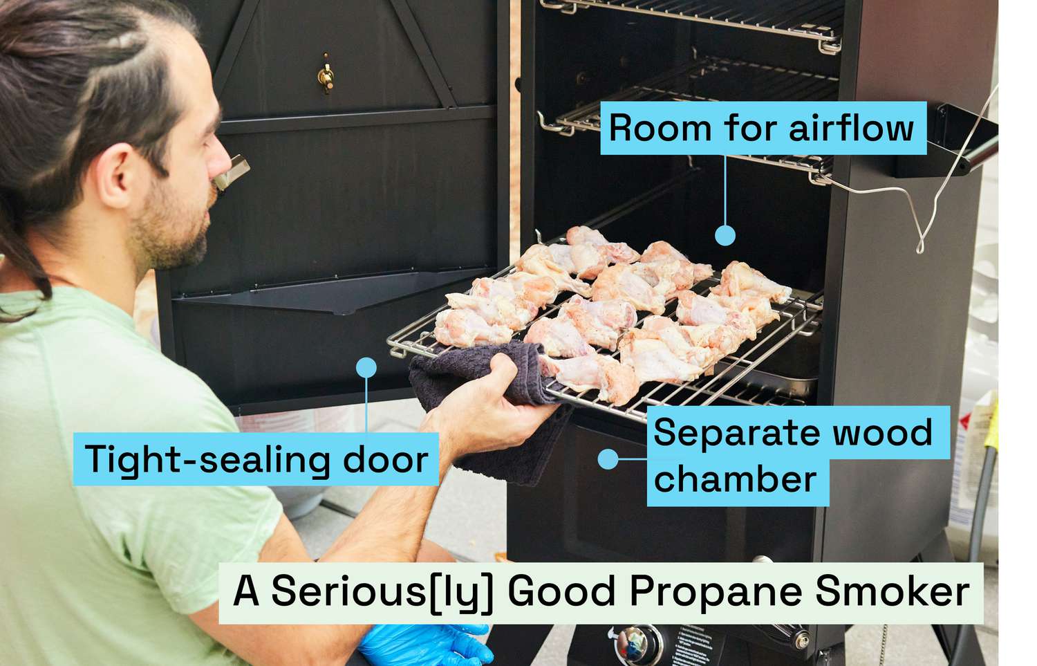 A person putting a rack of chicken wings into a propane smoker