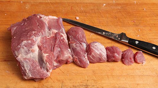Pork shoulder cut into different size chunks, from 1 pound to a half an inch on a wood cutting board, arranged from largest to smallest.