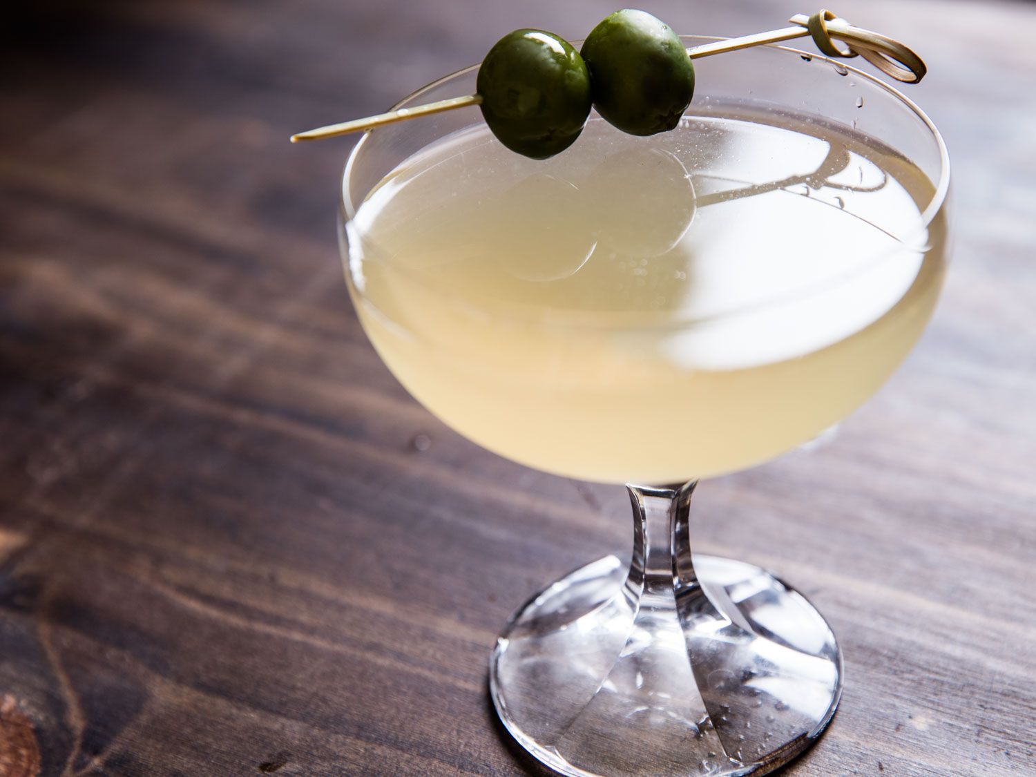 Dirty mezcal martini in a coupe glass with two skewered olives perched on the rim