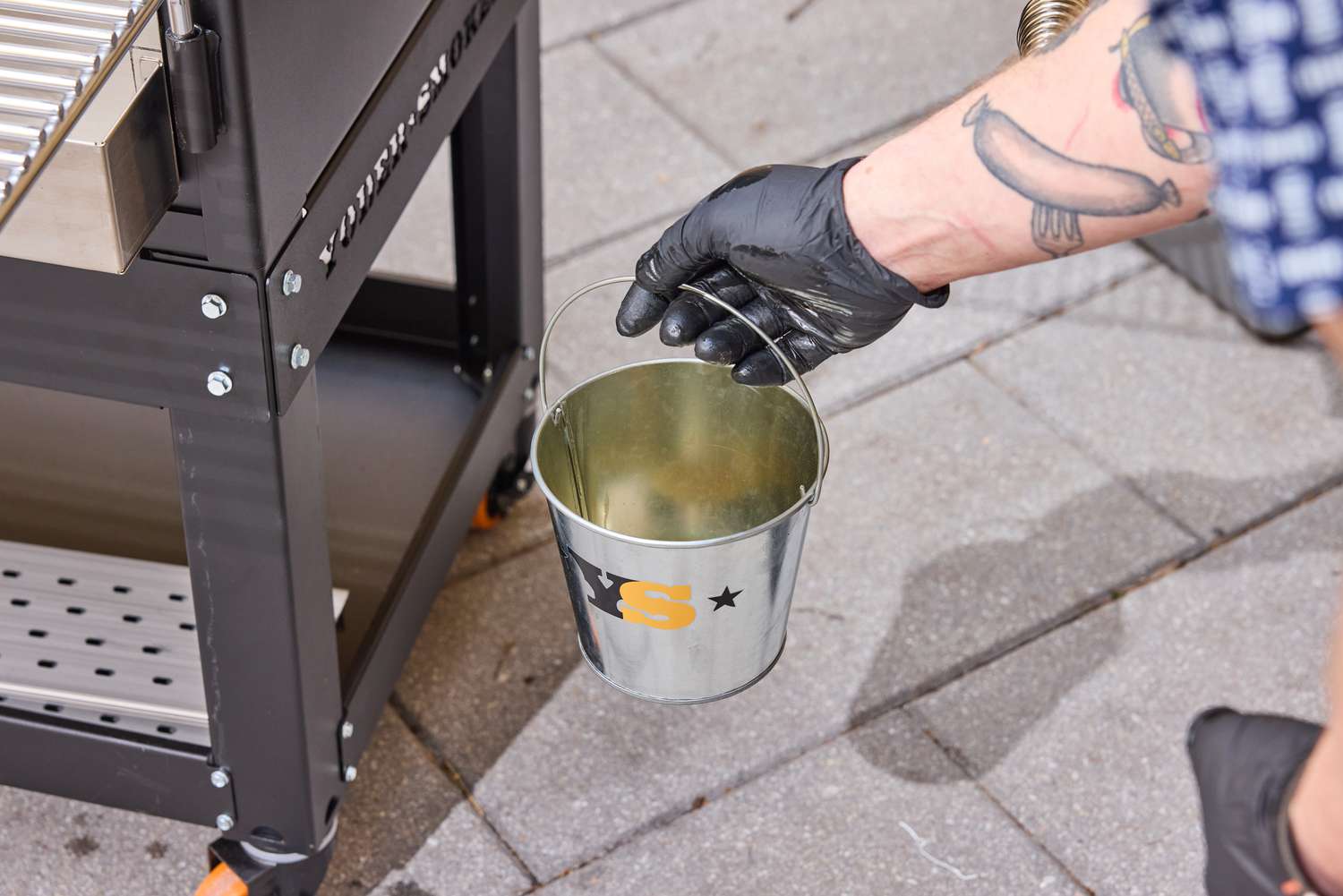 A person removes grease from the Yoder Smokers YS640S Pellet Grill