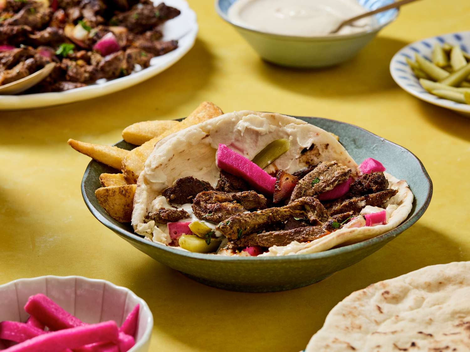 Beef shawarma wrap with pickles and side dishes on a table