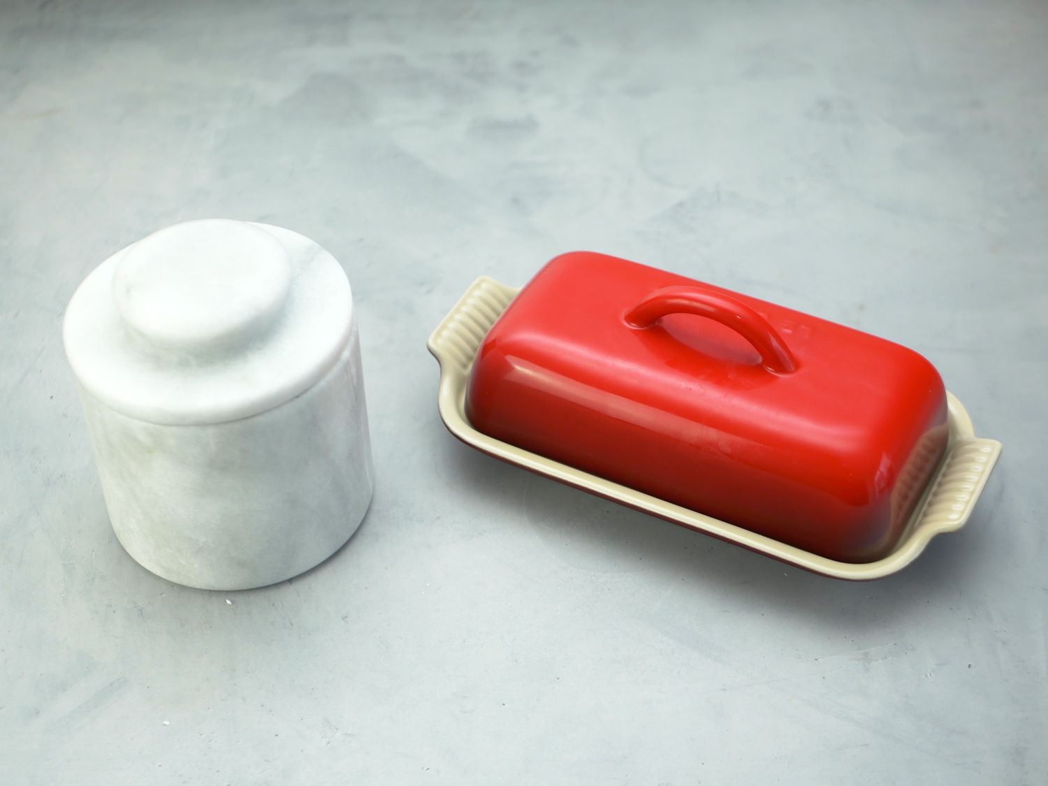 a marble butter bell next to the red le creuset butter dish on a gray surface