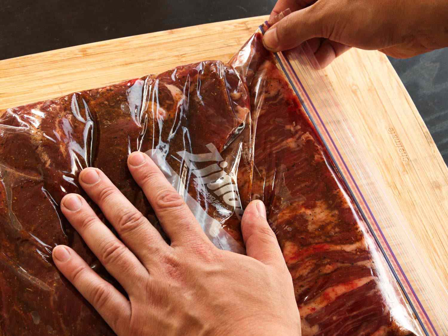 Hands sealing a plastic zipper-lock bag full of marinating skirt steak for fajitas.