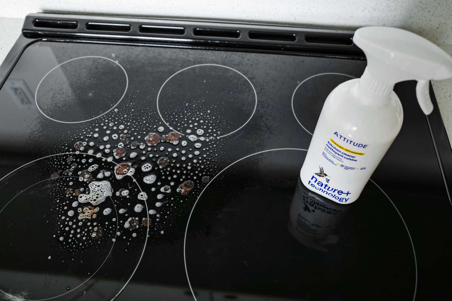 A stovetop with cleaning product applied a spray bottle labeled ATTITUDE placed on the surface