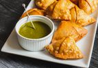Samosas on a serving plate with a ramekin of herb chutney alongside