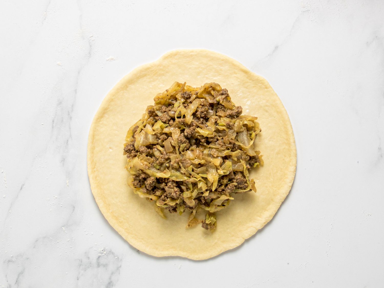 Filling placed in the center of rolled out dough on a white marble surface 