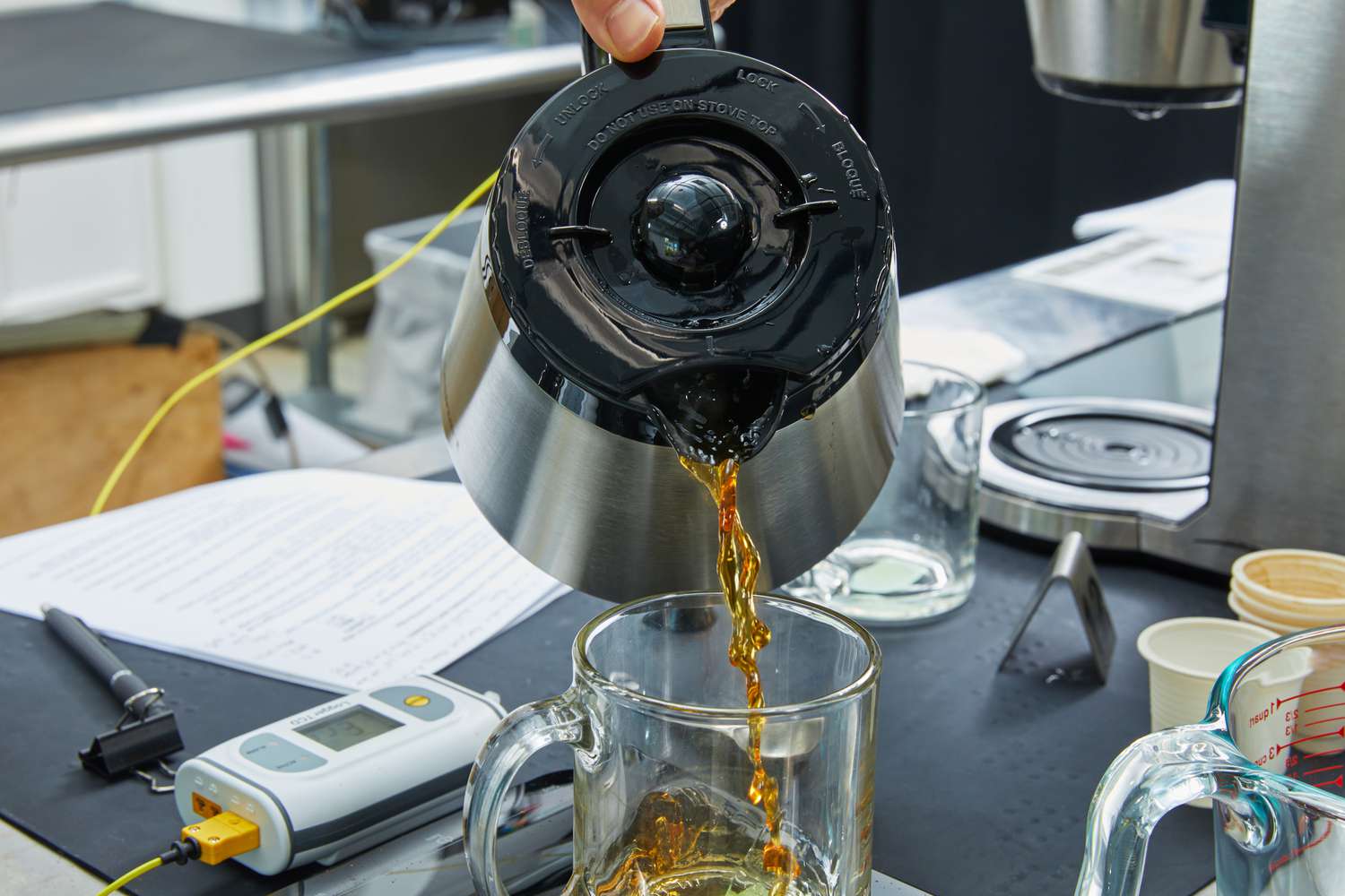 a person pouring from a thermal carafe into a glass coffee mug