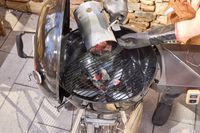 A hand emptying hot coals into the SNS Grills Slow 'N Sear Original 22-Inch Kettle Grill