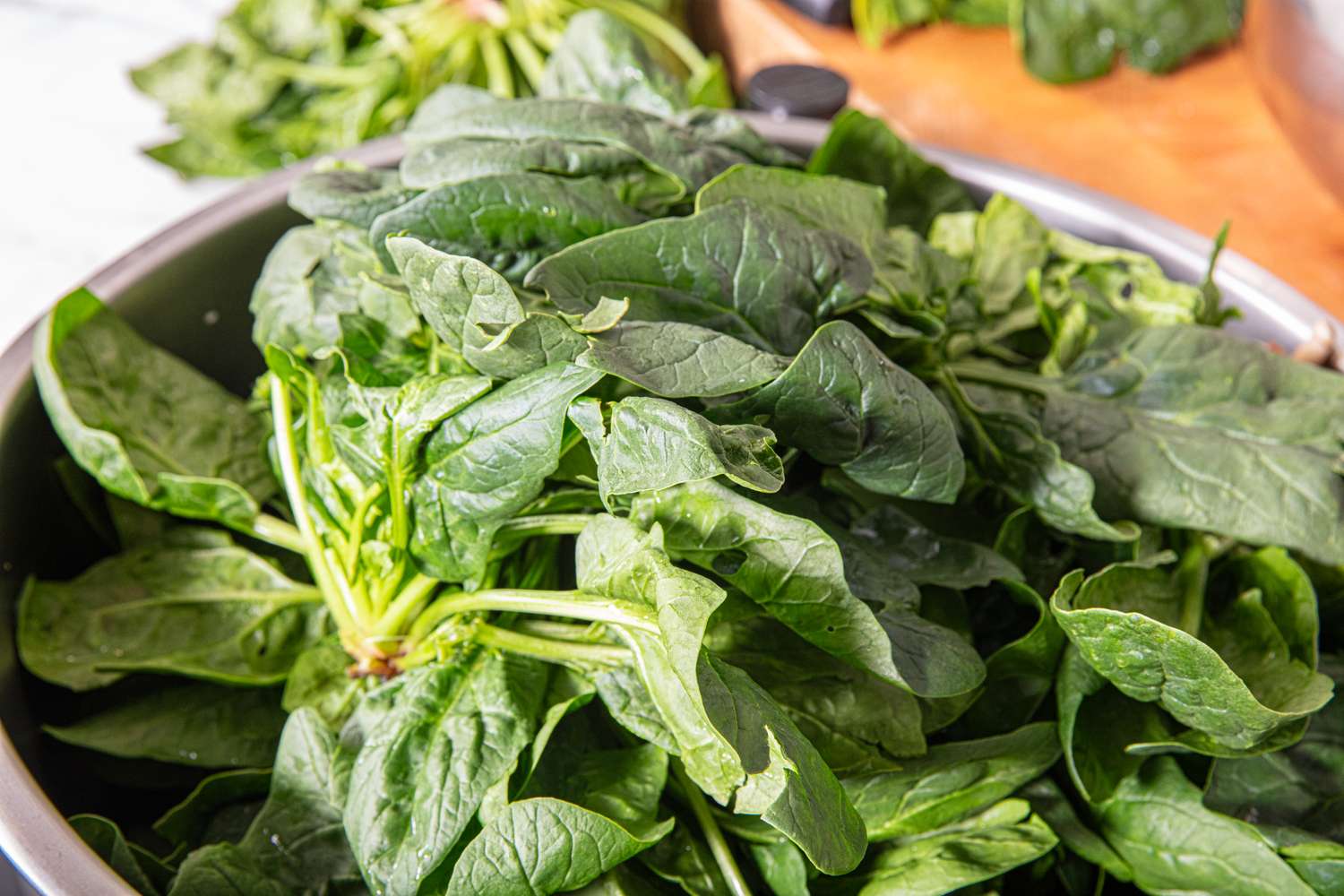 A bowl of fresh spinach leaves placed on a counter