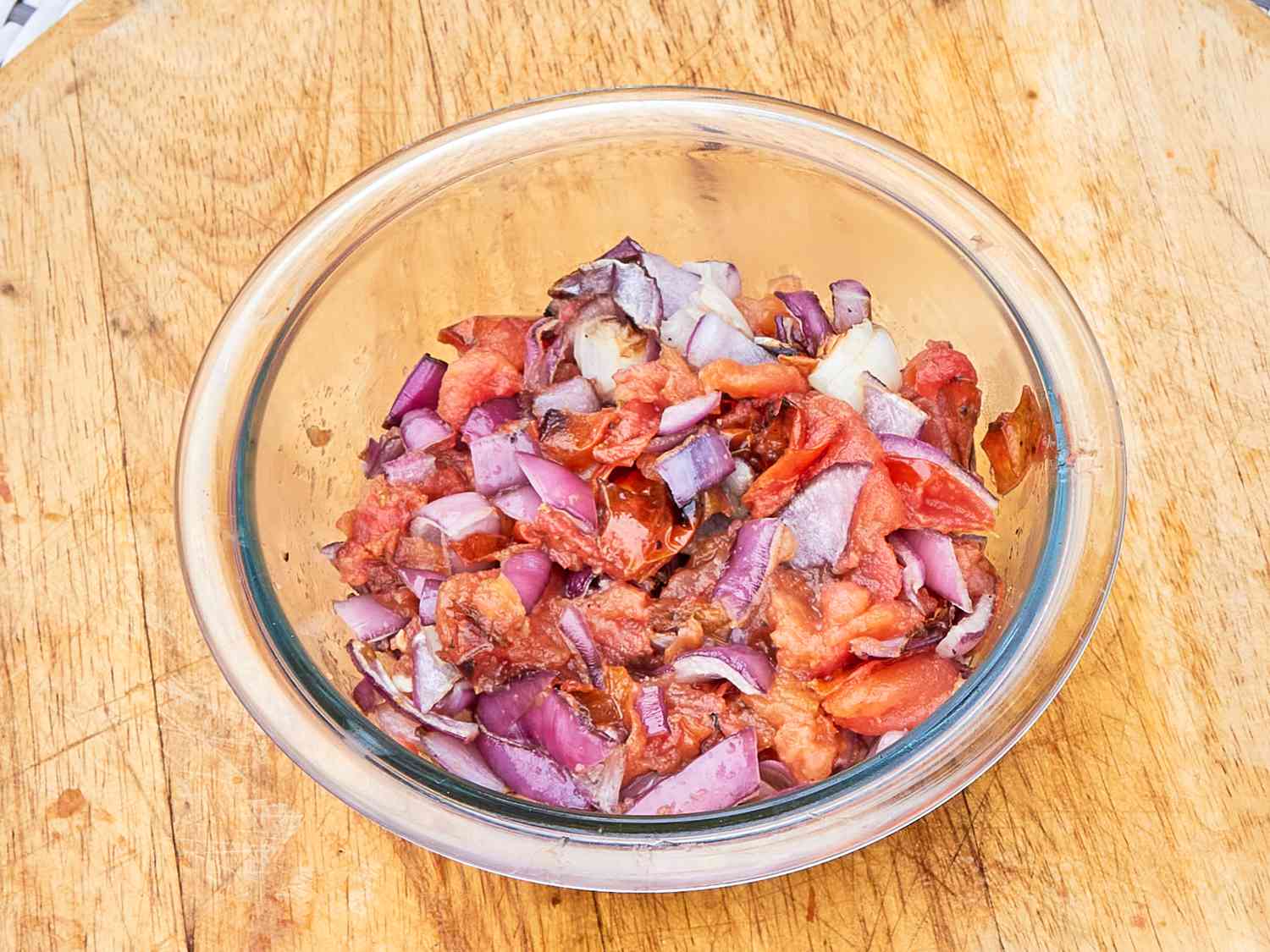 Chopped tomatoes and onions in a glass bowl on a wooden surface