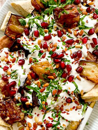 A plated serving of eggplant fatteh garnished with pomegranate seeds parsley and yogurt sauce