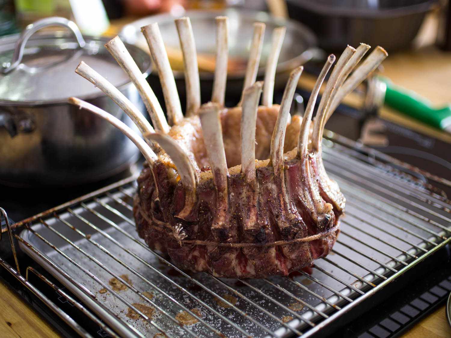 An uncooked, seasoned crown roast of lamb on a wire rack set over a baking sheet.