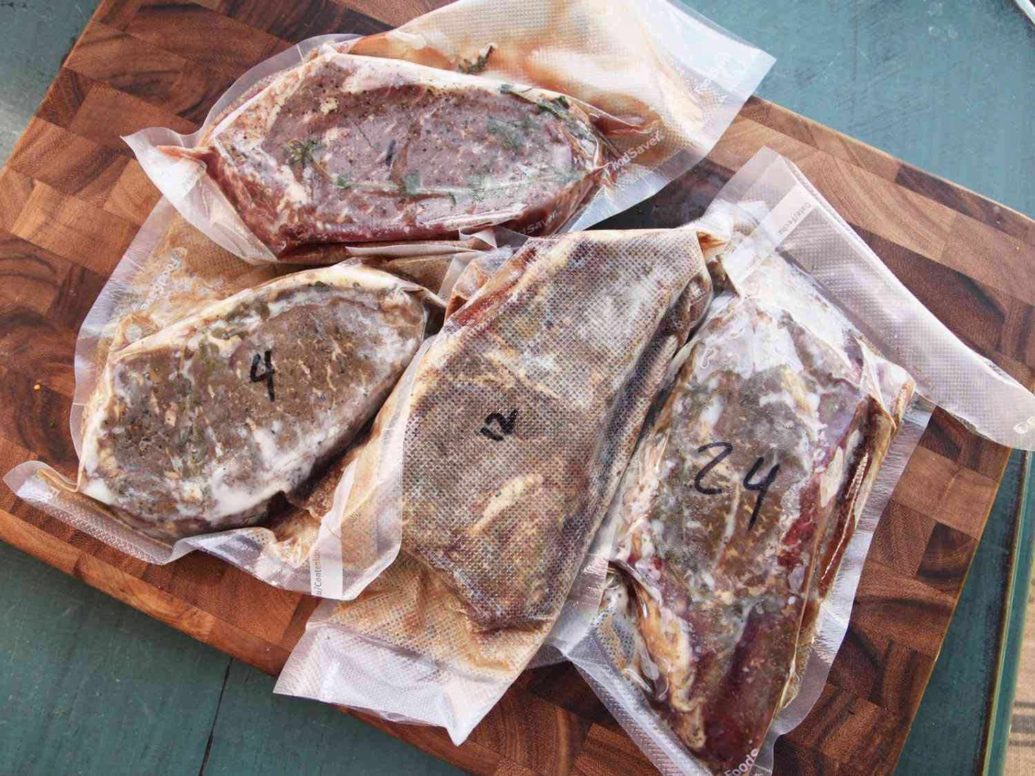 Overhead of four steaks vacuum-sealed in sous vide bags, resting on a cutting board. 