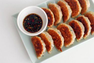 Crispy pan-fried vegetable dumpling arranged in rows on a plate with a dish of soy dipping sauce