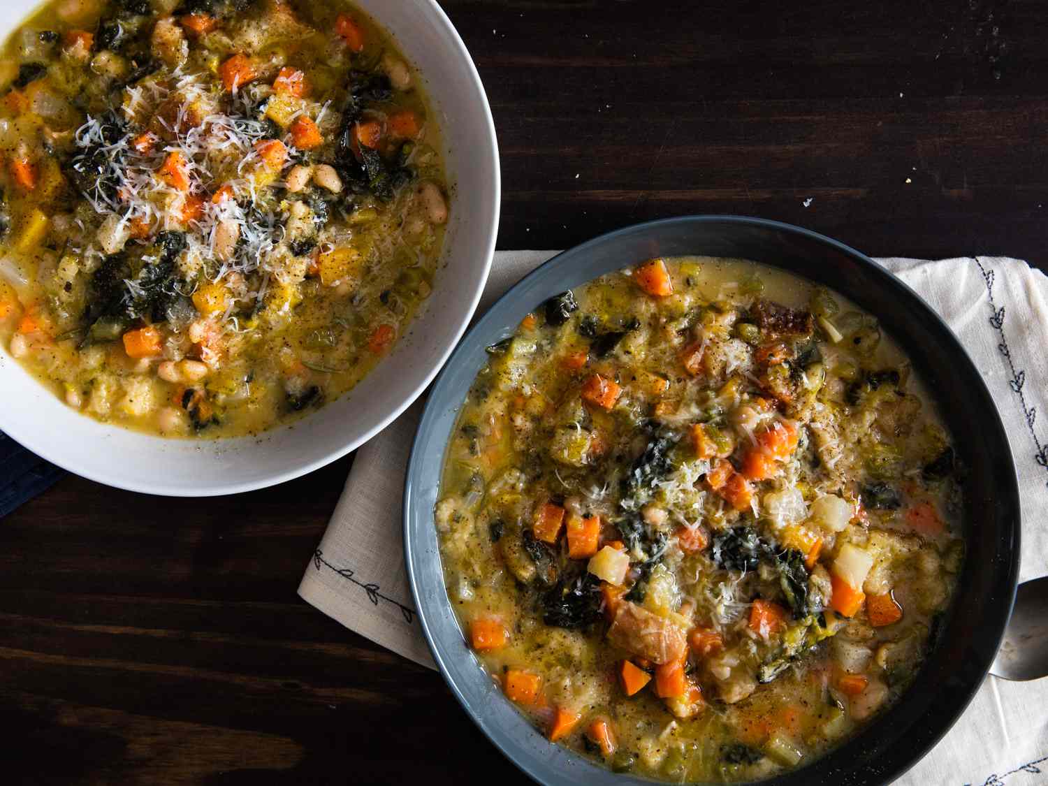 two bowls of Ribollita (Hearty Tuscan Bean, Bread, and Vegetable Stew) on a dark wood table. 