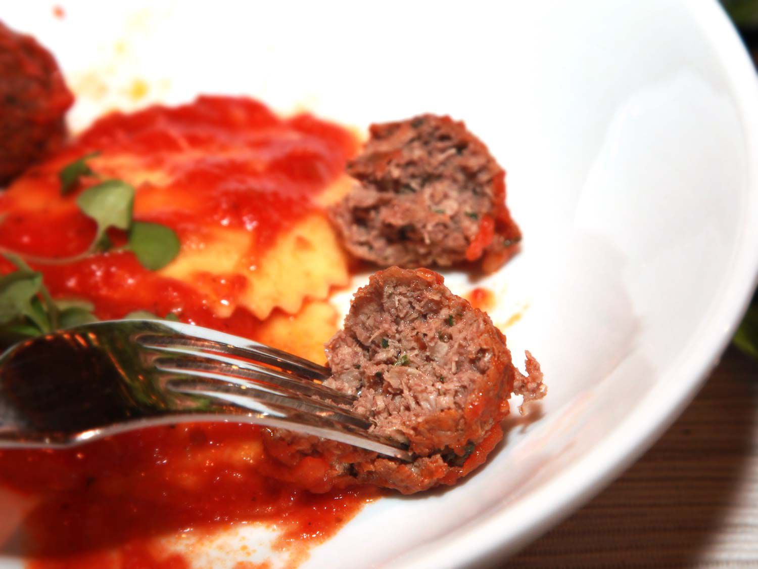Meatballs made of Impossible Burger on a plate with ravioli and tomato sauce. A fork is picking up one meatball. 